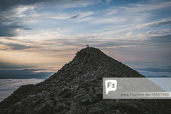 two tiny figures stand on summit of Mount Katahdin  Maine  sunrise