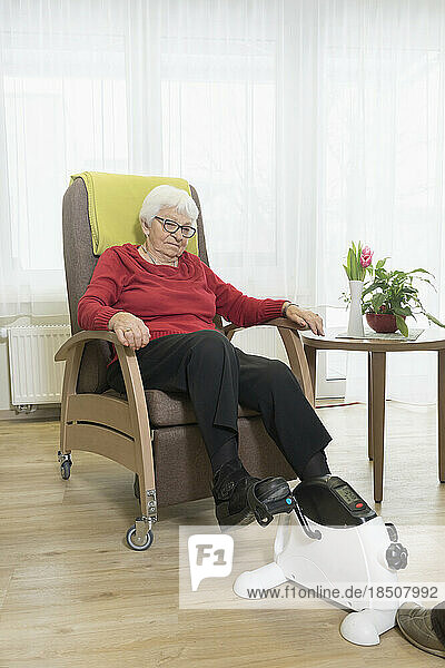 Senior woman doing exercise on mini foot pedal exerciser in rest home