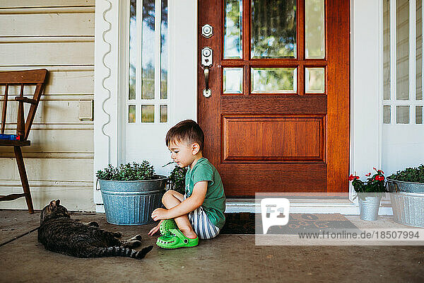Young boy sitting outside front door petting short hair cat