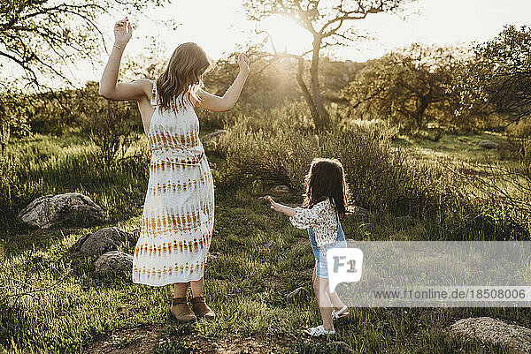 Young mother and daughter dancing in sunlight in bright field