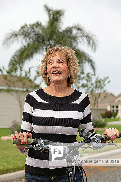Mature woman in her seventies laughing outside on her bike.