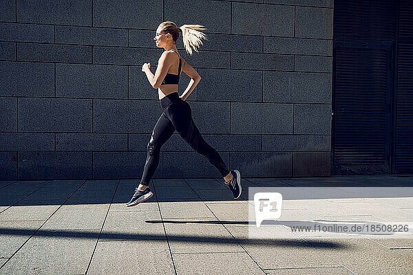 Woman in black sportswear jumping outdoors in front of wall