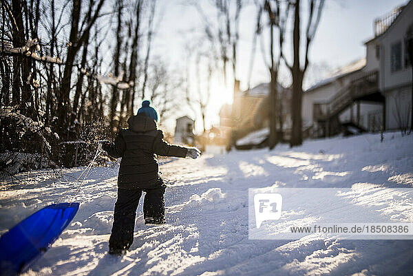 boy walking away into the sunset pulling blue sled behind him up hill