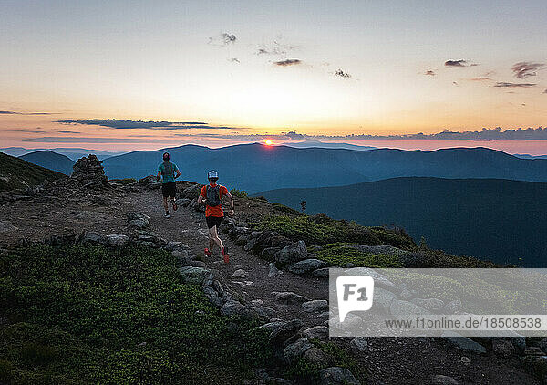 Two trail runner men running a path at sunrise with mountains