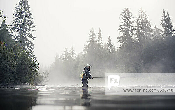 A man fly fishing in fog with trees behind
