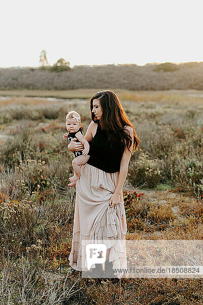 bohemian mom and baby girl on her hip in a field at sunset
