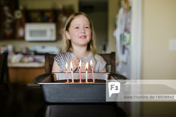 Candles on birthday cake 5 year old girl smiling in background