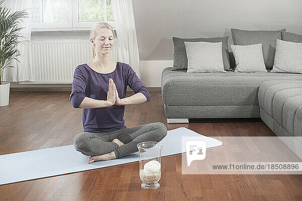Young woman doing lotus pose yoga on exercise mat in living room  Bavaria  Germany