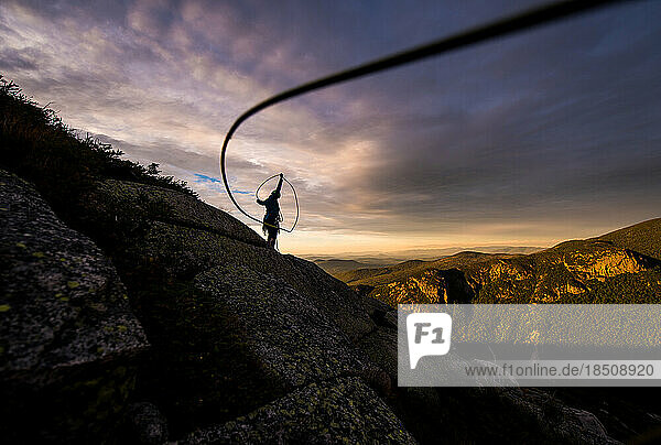 Woman coiling climbing rope at sunset on top of mountain