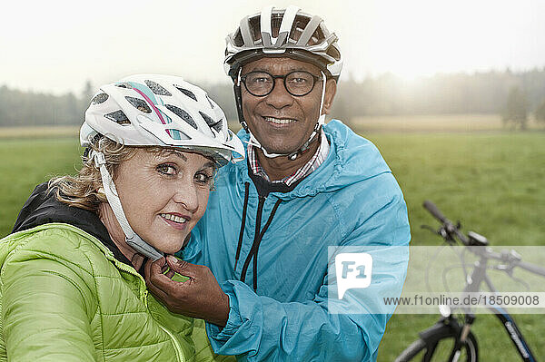 Senior man fastening on bicycle helmet to his wife and smiling  Bavaria  Germany