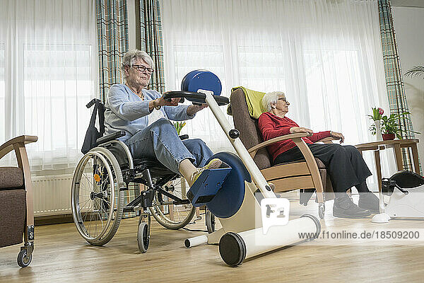 Two senior woman exercising on exercise bike in rest home