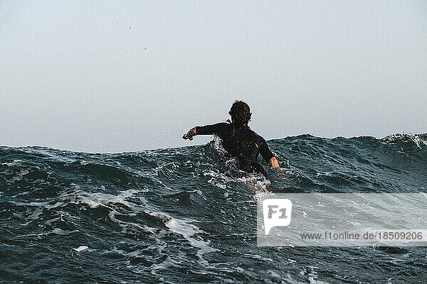 A male surfer paddles on moody sea
