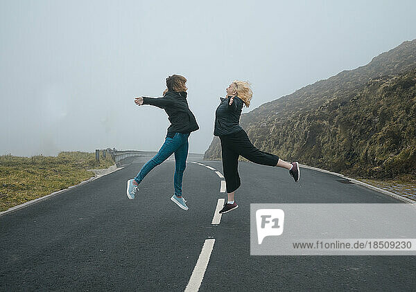 Two young women jumping on a road with fog