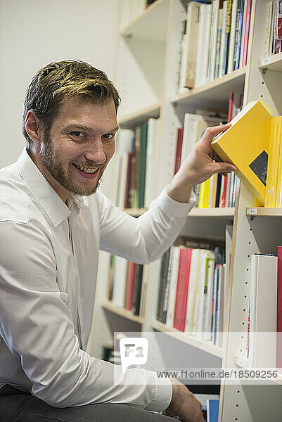 Portrait of a mid adult businessman choosing books from bookshelf in an office  Bavaria  Germany