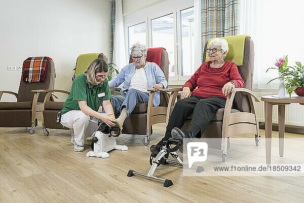 Nurse helping senior women doing exercise on mini foot pedal in rest home
