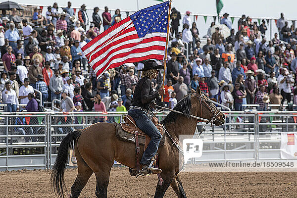 A rider carries an American flag opening the Arizona black rodeo