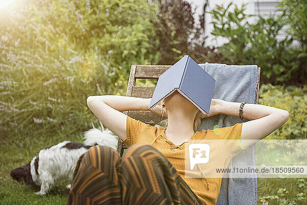 Beautiful young woman covering her face with a book and relaxing in the domestic garden  Munich  Bavaria  Germany