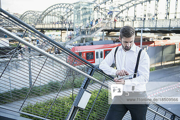 Businessman standing against railing and working on digital tablet  Munich  Bavaria  Germany