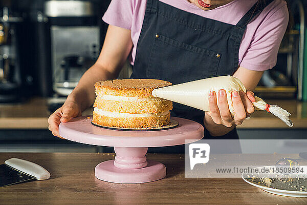Woman's hands in black apron decorate cake  squeezes out vanilla cream on a side of a cake
