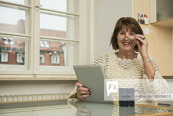 Portrait of a senior woman using a digital tablet and smiling in the kitchen  Munich  Bavaria  Germany