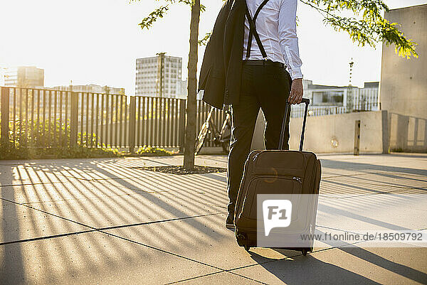 Rear view of a businessman pulling wheeled luggage at sunset  Munich  Bavaria  Germany