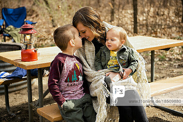 Smiling mother cuddles sons camping in fall picnic area