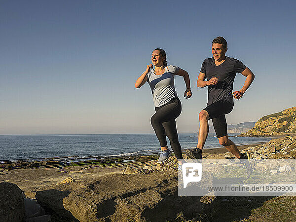 Man and woman running on single trail on coast of Azkorri beach
