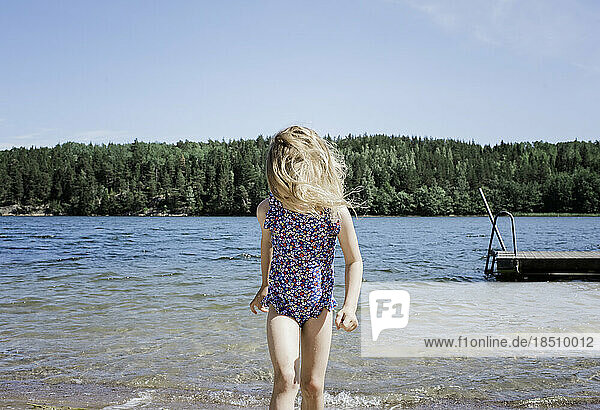 young blonde girl walking through the water at the beach in summer