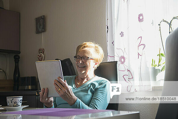 Happy old woman watching digital tablet at dining table