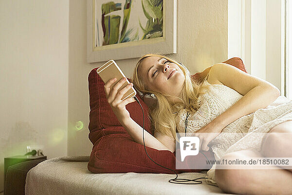Beautiful young woman listening to music and relaxing on sofa in the living room  Munich Bavaria  Germany