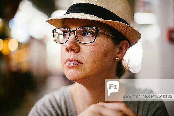 Woman in prescription glasses and hat looks thoughtful