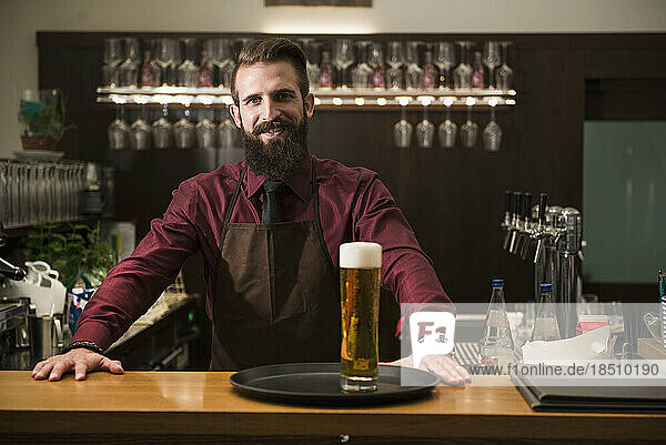 Portrait of young man at bar counter with glass of beer in tray