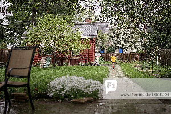 A small child stands in rain at end of long path in backyard