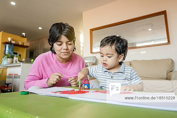 Latin mother and little son painting together with tempera colors.