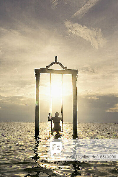 Rear view of woman sitting on rope swing at beach against sunset  Gili Trawangan  Lombok  Indonesia
