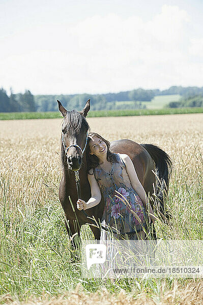 Mature woman standing with her brown horse on wheat field and smiling  Bavaria  Germany