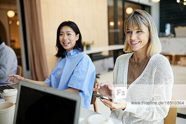 Happy female businesswoman with smart phone by coworker at cafe