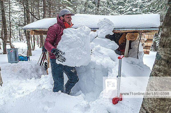 Man shoveling snow in front of cabin in winter