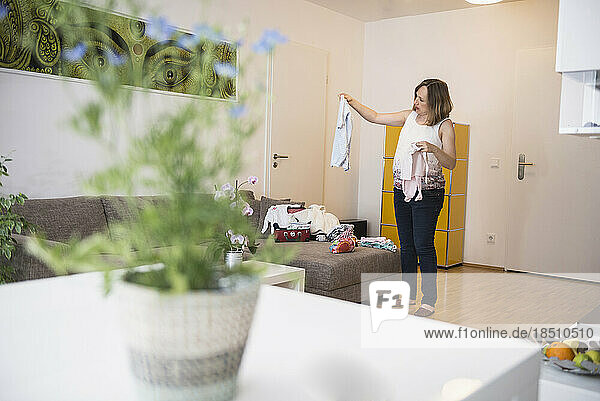 Pregnant woman standing in living room and looking at baby clothes  Munich  Bavaria  Germany