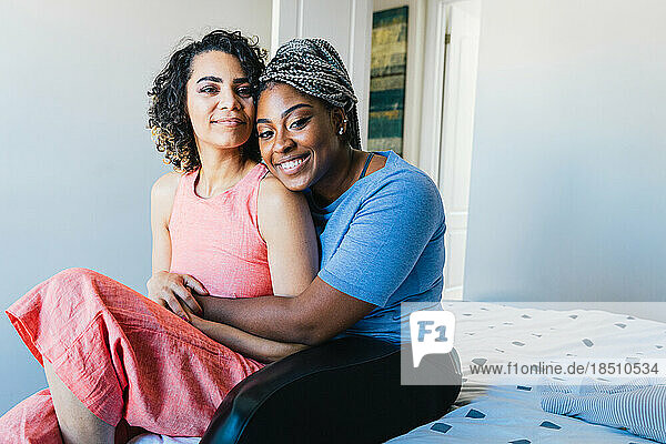Portrait of confident happy lesbians sitting on bed at home