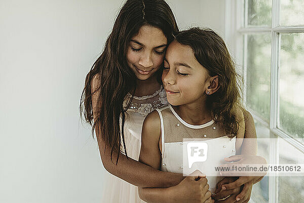 Sisters hugging in natural light studio while closing eyes