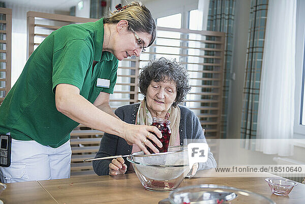 Nurse preparing dessert with senior woman in rest home