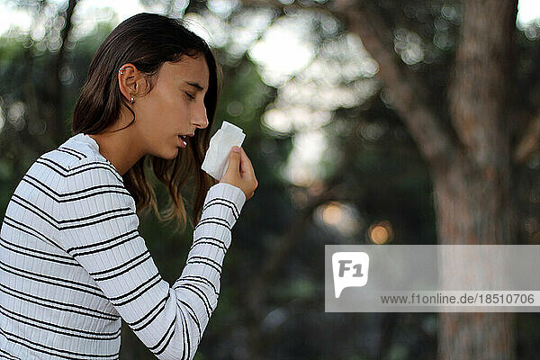Health and medicine - Young woman sneezing in the woods.
