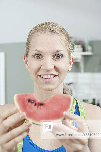 Young woman eating slice of watermelon in the kitchen and smiling  Bavaria  Germany