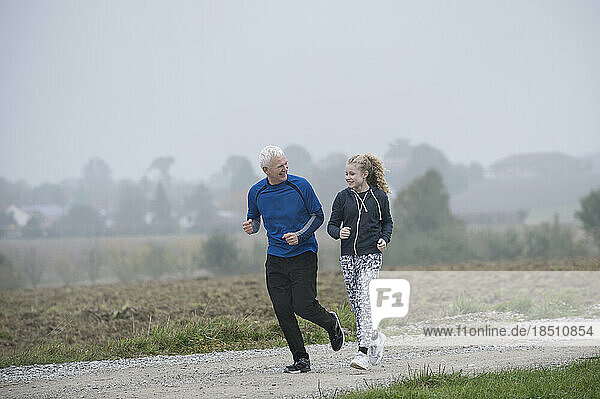 Father with his daughter jogging on footpath and smiling during dawn  Bavaria  Germany