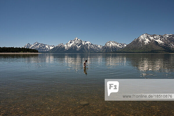 Teen girl standing in lake near Grand Tetons on sunny day