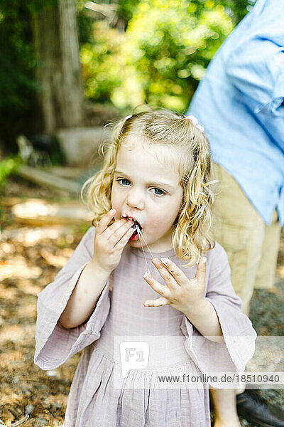 Straight on view of a young girl eating a messy marshmallow s'more