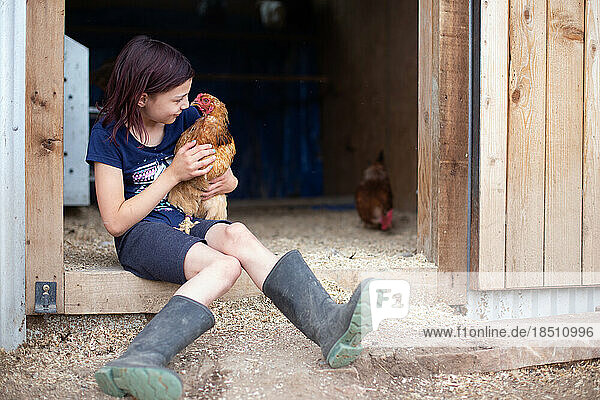 Girl sitting with chicken outside coop