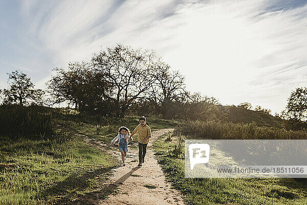 Brother and sister holding hands and running in backlit field