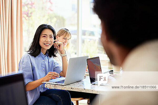 Happy female professional sitting with laptop at table in cafe